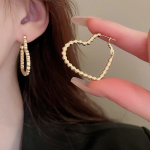 Detail of golden heart-shaped earrings with scalloped edges and polished finish