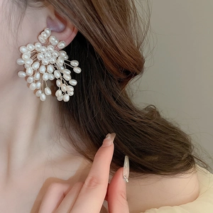 Close-up of elegant floral burst earrings with white pearls and gold wire on a model