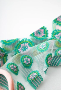 Detailed close-up of light green mesh hair tie with vintage pink floral embroidery