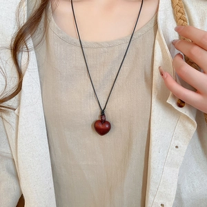 Close-up of heart-shaped wooden pendant with black cord on beige linen fabric