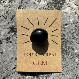 Polished black gemstone on a You're a Real Gem kraft card over natural stone