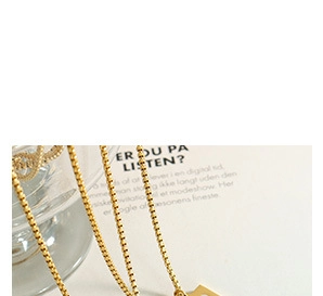 Minimalist gold box chain necklace with geometric pendant on a magazine background