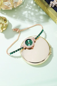 Detail of luxury gold bracelet watch with green gemstone accents and crystal bezel