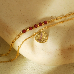 Elegant gold double layer heart bracelet with red stones and pink crystals on stone surface