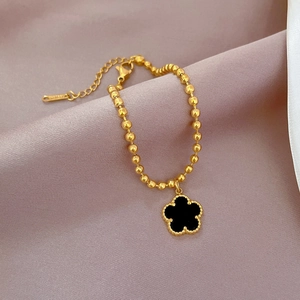 Macro shot of gold beaded bracelet featuring a black clover charm and S-STEEL hallmark