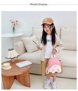 Toddler girl wearing pink canvas backpack with plush long-ear bunny on soft sofa