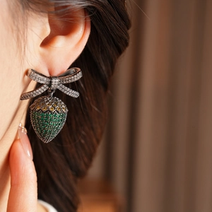 Macro view of vintage strawberry drop earring with rhinestone bow on person