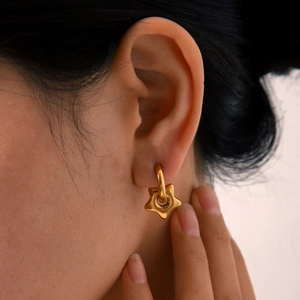 Detail of gold-tone star pendant earring on model showing polished finish and drop design