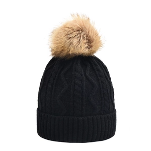 Close-up of black cable knit pattern and large brown faux fur pom pom on a winter beanie
