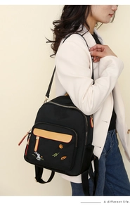 Side view of woman wearing black and beige color-block nylon backpack with embroidery