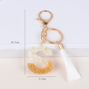 Detail showing letter S keychain with gold foil, white shell flakes and white tassel