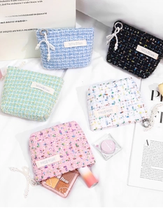 Detailed view of tweed cosmetic bags in five colors with pearl zipper charms and textures