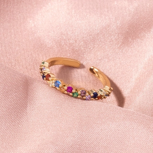 Detail view of gold open ring with colorful zircon stones on soft pink fabric