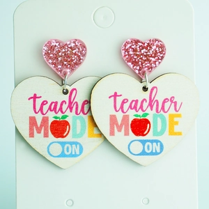 Detail of heart-shaped wooden earrings with teacher MODE ON print and pink glitter stud