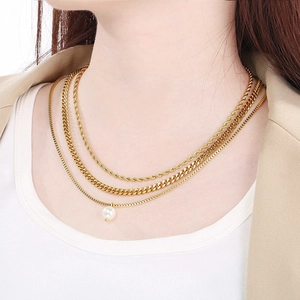 Close-up of triple-layered gold necklaces with cuban links, rope chain and pearl charm