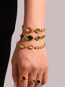 Close-up of stacked colorful oval glass stone bracelets and 18k gold rings on a model hand