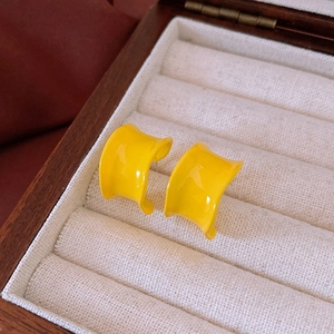 Close-up of bright yellow wide curved wave earrings displayed in a wooden jewelry box