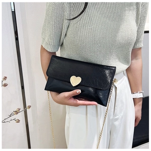 Close-up of black patent leather rectangular clutch with gold heart clasp and chain strap