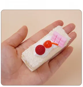 Realistisches Mousse-Tortenmodell mit Kirsch-Deko in der Hand zum Größenvergleich