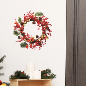 Christmas wreath with red berries and pine cones hanging on white wall for home decor
