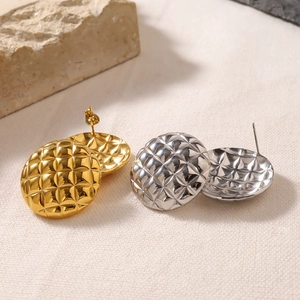 Macro detail of gold and silver stainless steel earrings with rhombic texture on linen