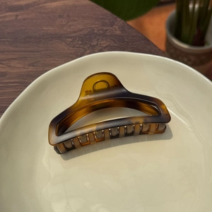 Macro detail of amber tortoise shell hair claw clip with glossy finish on ceramic plate