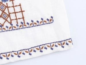 Detailed close-up of brown and purple floral embroidery on white V-neck shirt fabric