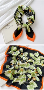 Detail of silk-feel square scarf featuring orange floral patterns on a black background