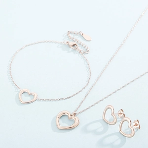 Detailed view of rose gold hollow heart necklace, bracelet, and earrings set on blue background