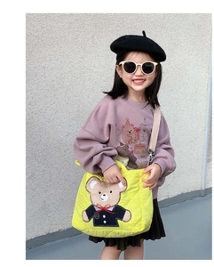 Detail of yellow quilted crossbody bag with bear patch and purple cotton sweatshirt