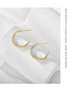 Detailed view of gold plated twisted C-shape earrings on a white geometric stand