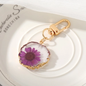 Detail of a purple dried flower resin keychain with gold serrated edges on white bone china