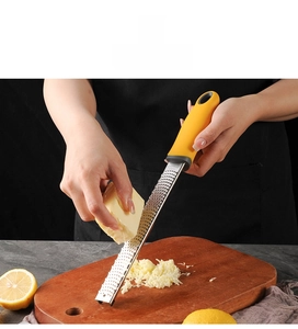 Close-up of stainless steel cheese grater with yellow handle shredding fresh parmesan
