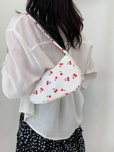 Detailed view of white nylon underarm bag featuring red cherry prints worn by a model
