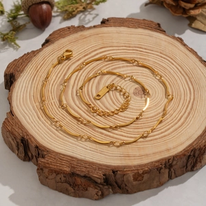 18K gold-plated stainless steel wavy chain necklace on a rustic wooden stand with pine cones