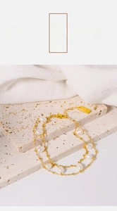 Macro detail of double-layer gold chain bracelet with freshwater pearls and a gold tag