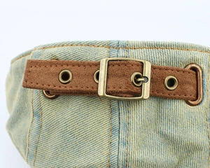 Detail of blue denim cap with brown faux suede strap and bronze metal eyelets