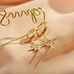 Detail of gold octagonal star hoop earrings featuring micro-pave zirconia on satin background