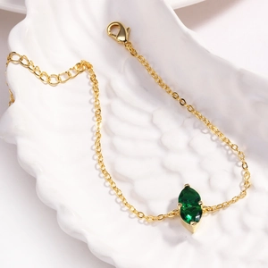 Detailed close-up of a golden bracelet featuring a marquise green gemstone on a shell tray