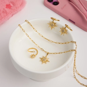 Close-up of gold sun-shaped jewelry set with necklace, ring, and earrings in a ceramic bowl