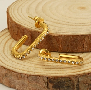 Detail of gold-plated U-shaped earrings with clear zircons on a natural wood slice
