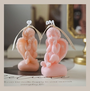 Close-up of two pink angel-shaped soy wax candles with ribbon details on a vintage desk