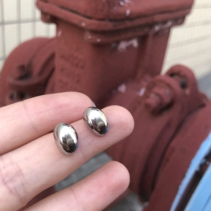 Close-up of small silver polished oval stud earrings held by a hand on a metal background