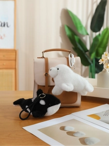 Detail of plush seal and orca whale keychain charms hanging on a leather handbag