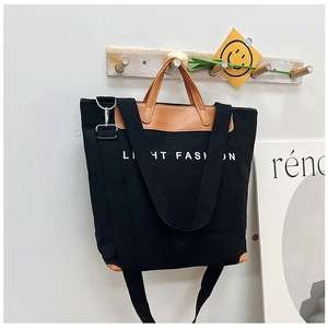 Detail of black canvas tote bag with brown leather accents and wide shoulder strap