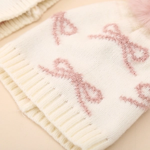 Close-up of knit texture and pink bow pattern on winter baby hat with faux fur pom