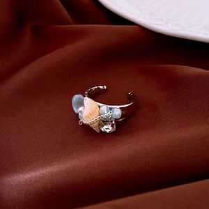 Close-up of Bohemian ocean shell ring with pearl and blue beads on silk background