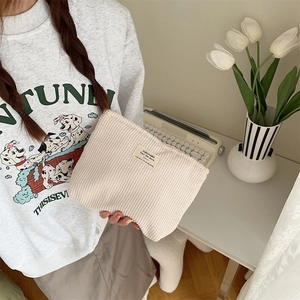 Detail of a beige corduroy makeup bag held by a model with a vintage aesthetic background