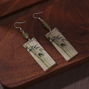 Detailed shot of Chinese style earrings with green beads and bamboo pattern on a wooden tray