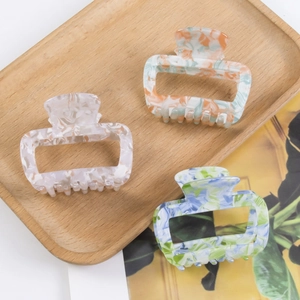 Marbled acetate hair claws in orange, purple and blue-green on a wooden tray